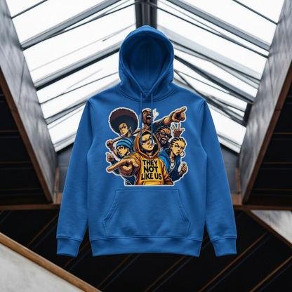 A mustard blue pullover hoodie with a colorful graphic print of cartoon characters and the text 'THEY NOT LIKE US' on the front, displayed against a modern architectural background with glass skylights.