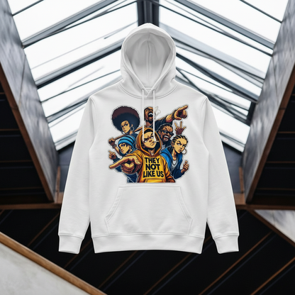A mustard yellow pullover hoodie with a colorful graphic print of cartoon characters and the text 'THEY NOT LIKE US' on the front, displayed against a modern architectural background with glass skylights.