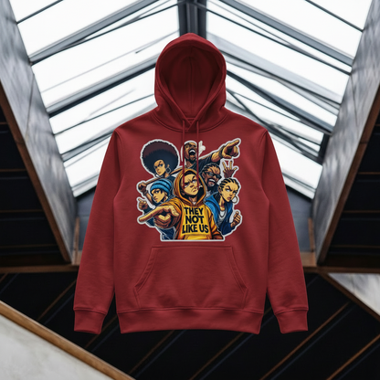 A crimson pullover hoodie with a colorful graphic print of cartoon characters and the text 'THEY NOT LIKE US' on the front, displayed against a modern architectural background with glass skylights.